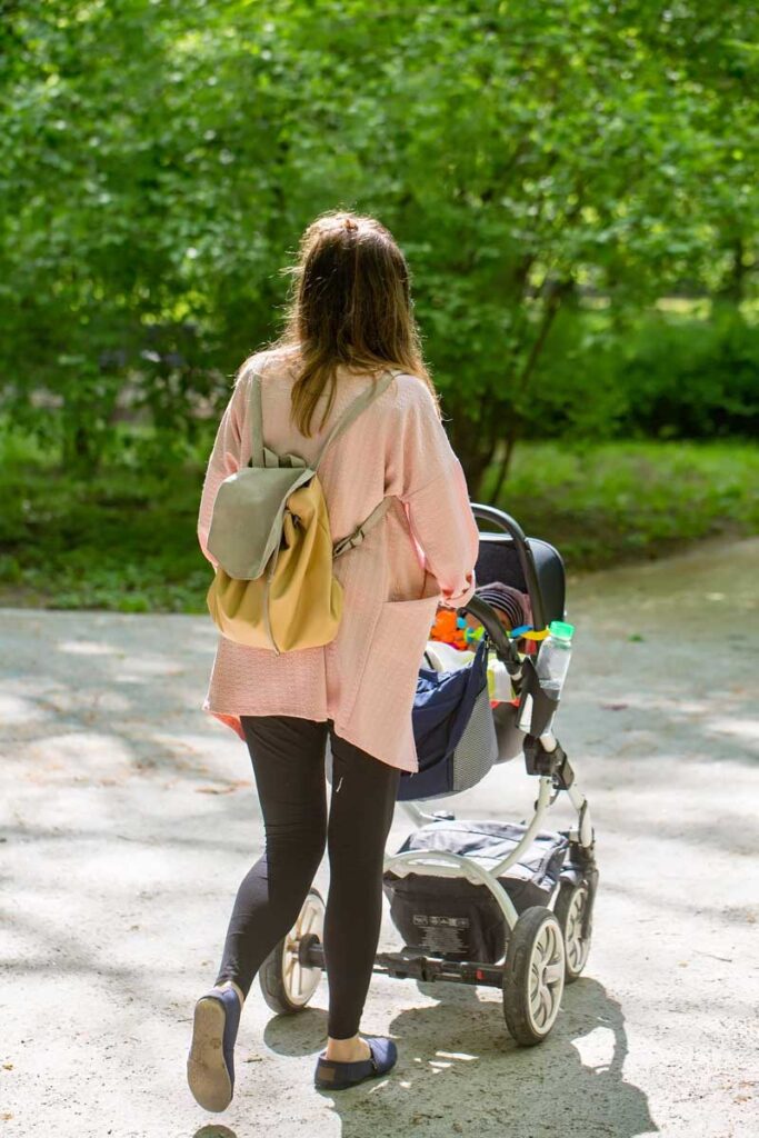 Woman pushing stroller carrying best baby backpack diaper bag